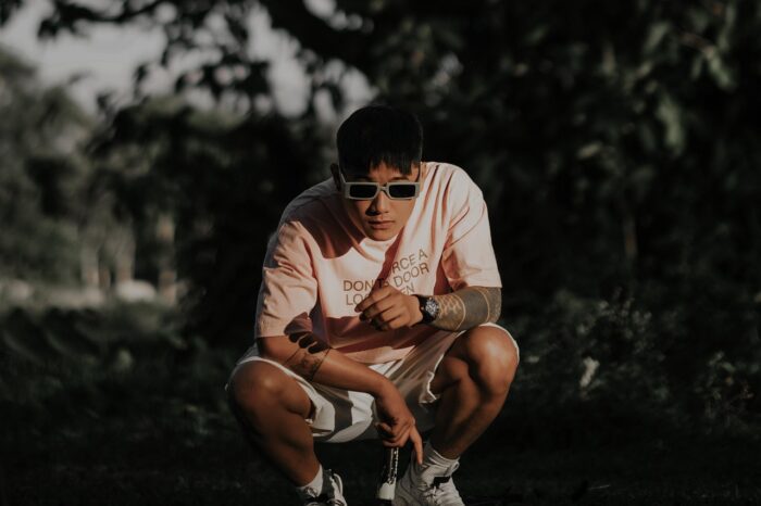 man crouching wearing sunglass, a pink tshirt and shorts